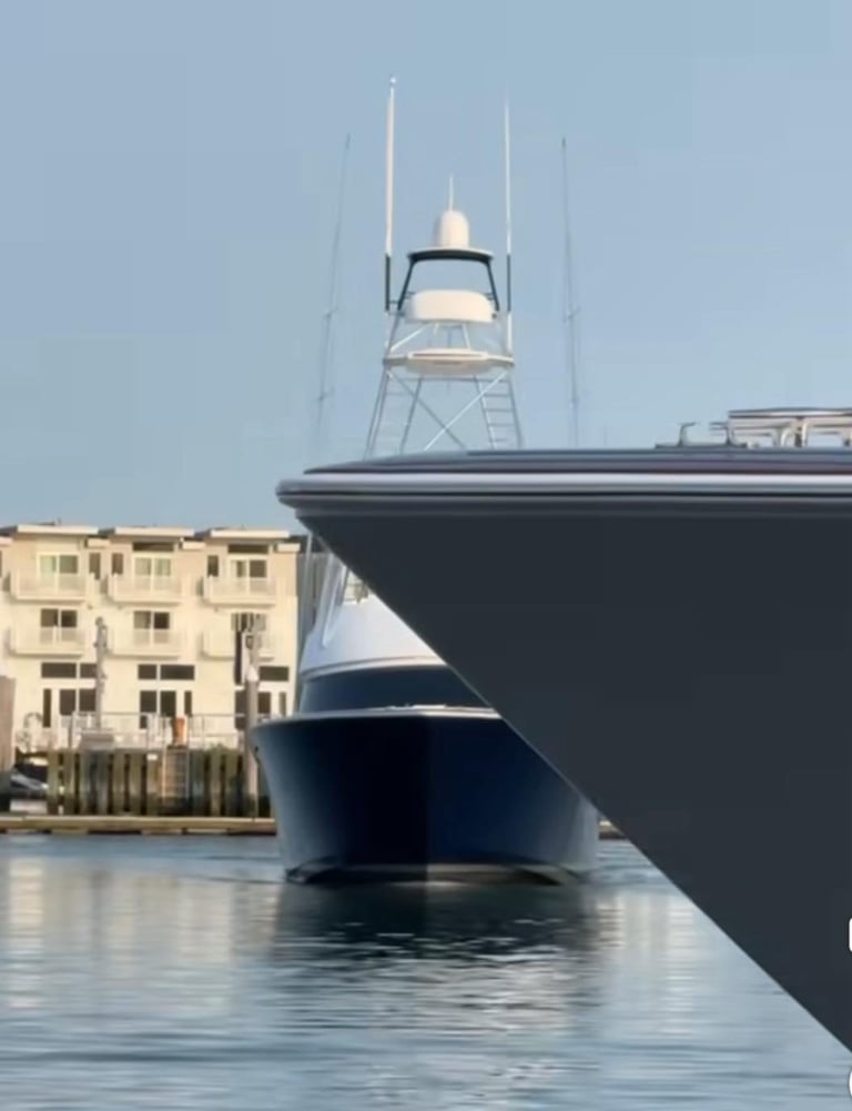 Large fishing yacht with blue hull docked at waterfront, cream-colored building visible behind in calm water