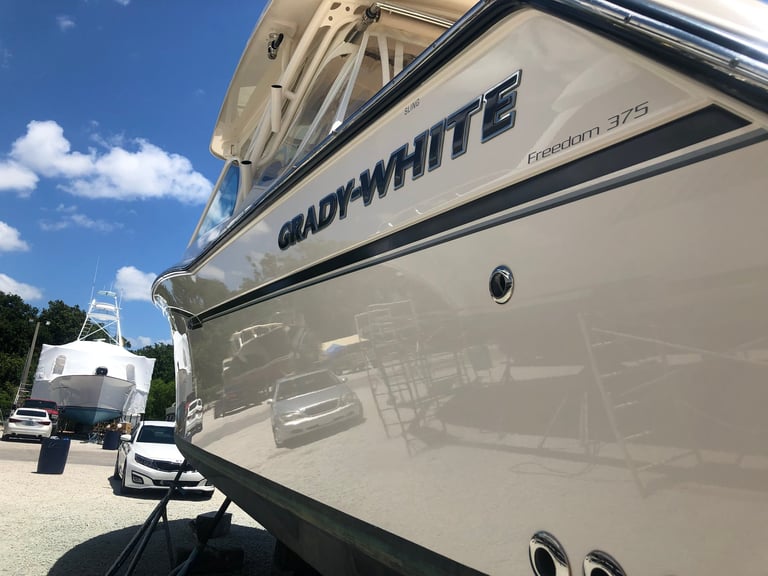 Grady-White boat hull displayed at dealership with clear blue sky and other vehicles in background