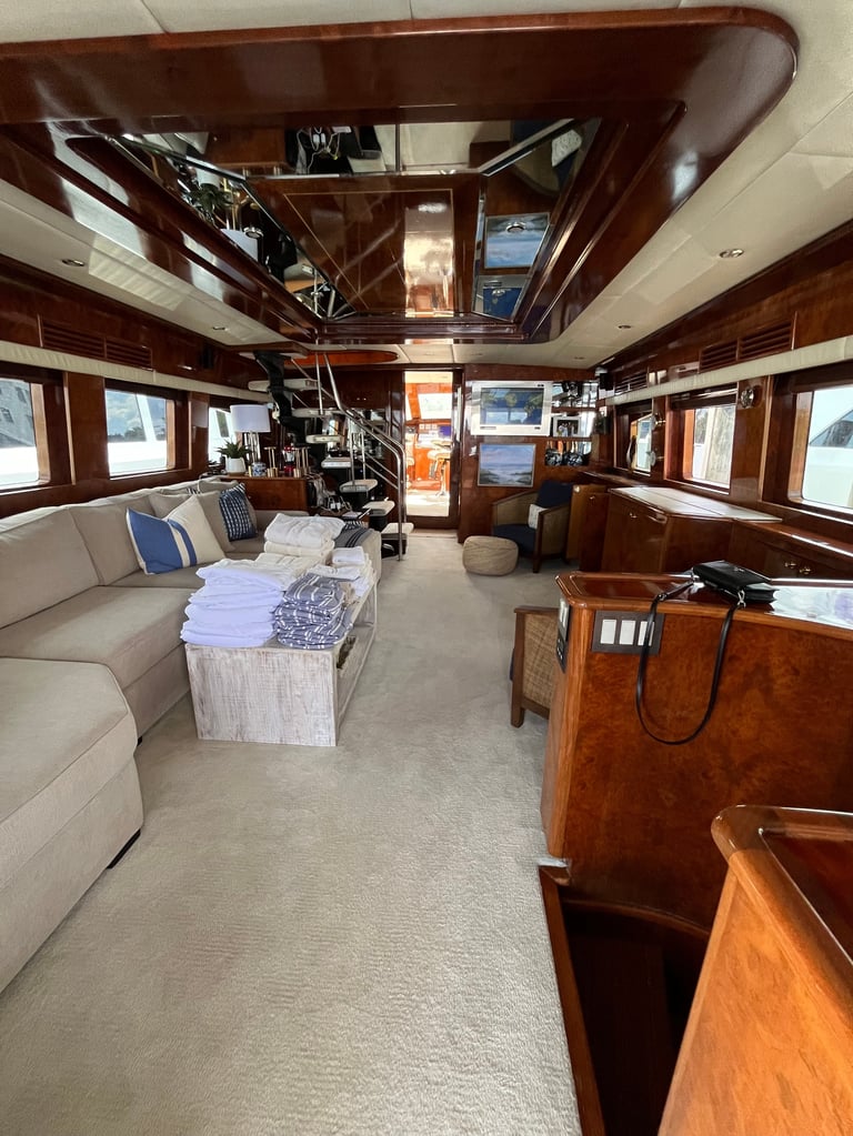 Interior of a luxury yacht with wood paneling, beige seating, cream carpet, and multiple windows showing ocean views
